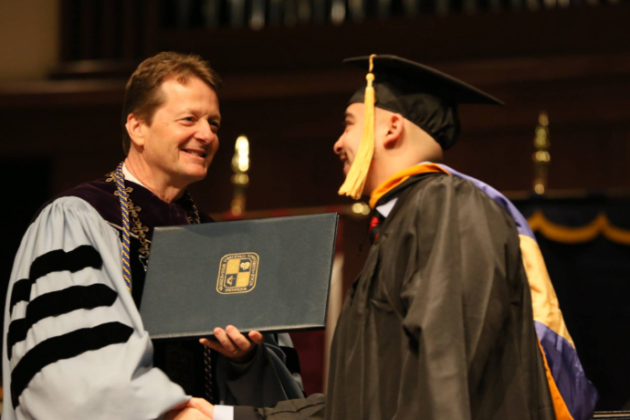 A photo of TXWES President Frederick G. Slabach handing a diploma to a graduate during Fall 2018 Commencement. 