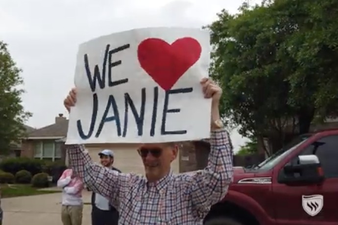 Photo of Professor Joe Brown honoring alumnae Janie Faris with a sign that says We Love Janie.