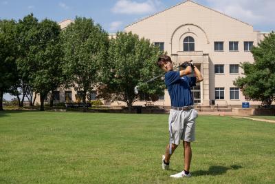 Jung Woo Youn practicing his golf swing with the West Library in the backgroubnd