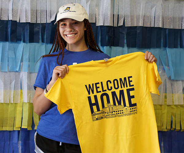 An excited student holding a yellow shirt with the words Welcome Home