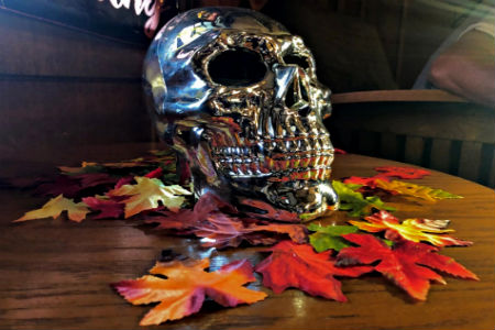 A silver skull sitting on a wooden table with fake leaves strewn about