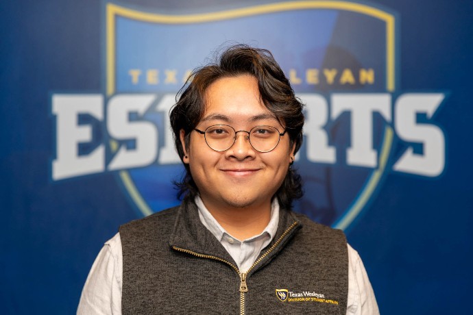 Assistant Director of Esports and Gaming, Michael Nguyen, poses in front of the Esports logo