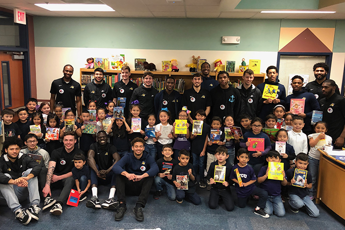 A group photo of first graders from Alice Contreras Elementary and the 2018-19 Texas Wesleyan Men's Basketball team. The students are holding their favorite books.