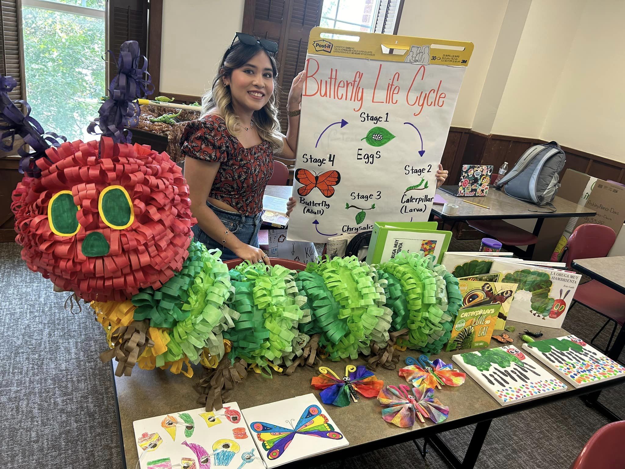 A female student stands behind her project of a piñata style caterpillar from The Hungry Caterpillar