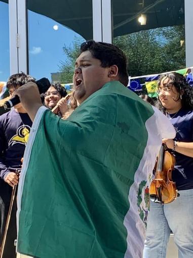 Student leading in song for Hispanic Heritage Month celebration wrapped in the flag