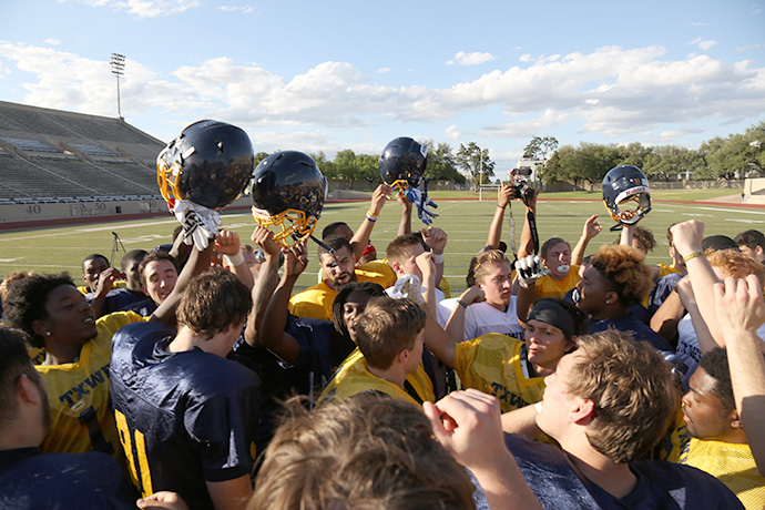Photo of TXWES football players with helmets raised.